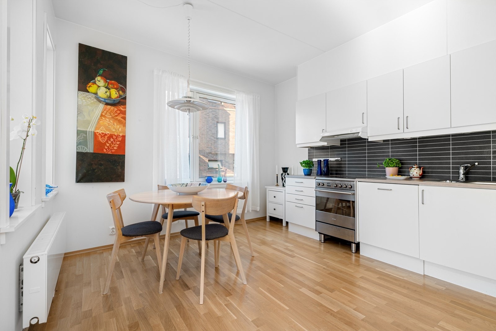 Tidløs kjøkkeninnredning med hvite, glatte fronter og laminat benkeplate. Fritstående kjøleskap med fryser, komfyr med keramisk topp og integrert oppvaskmaskin. Galleribilde
