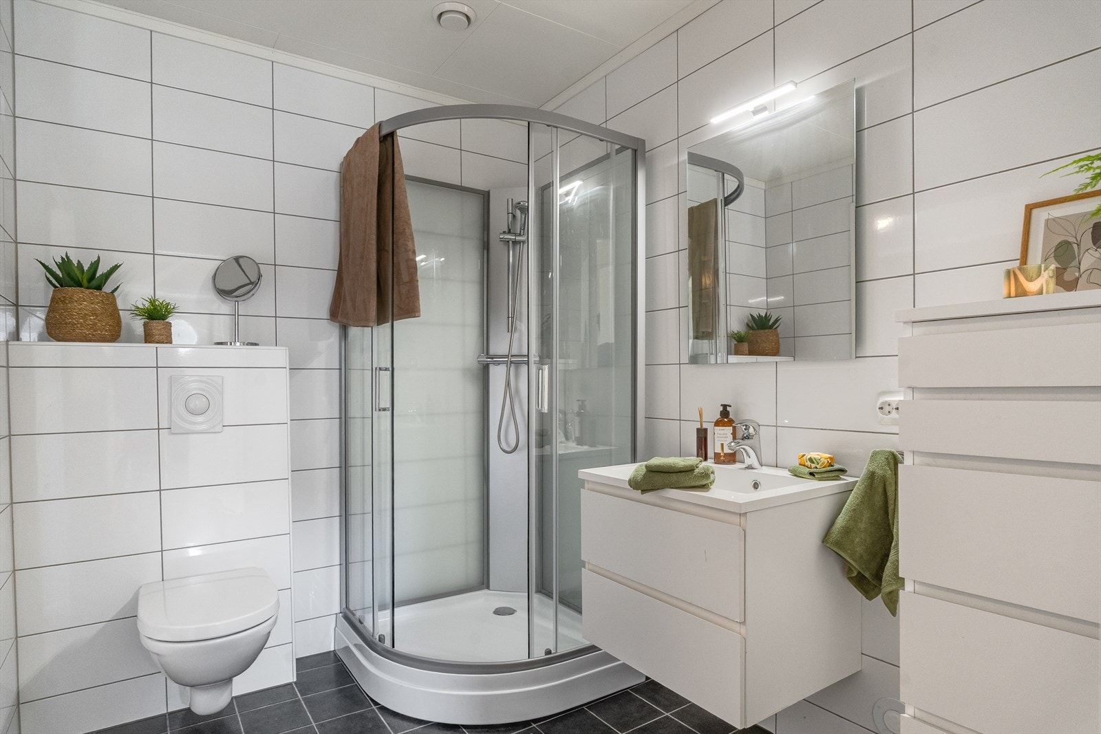 Flott, helfliset baderom med moderne innredning - hvit baderomsinnredning med speil og skap, vegghengt toalett og dusjkabinett. Det er varmekabler i gulv. Galleribilde