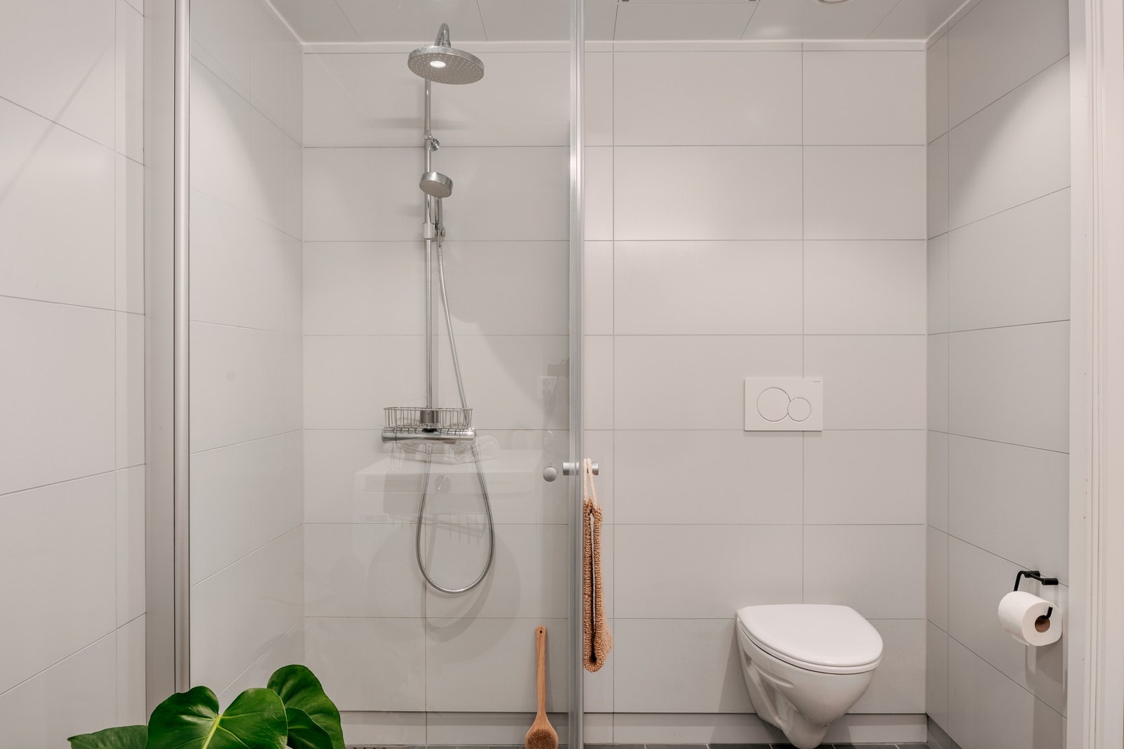 Badet er innredet med vegghengt toalett, dusj med glassvegger, og baderomsmøblement med speil og belysning. Galleribilde