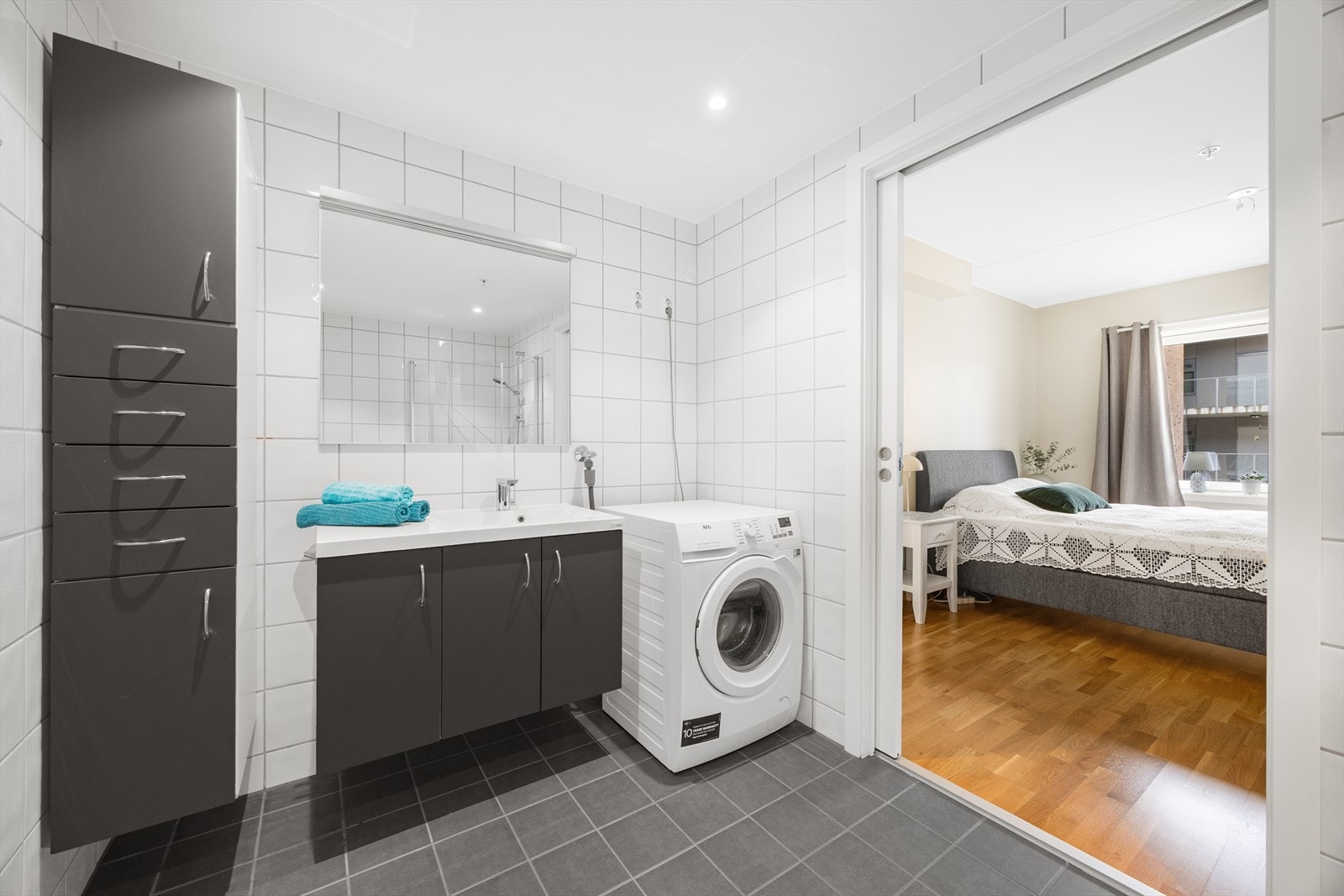 Badet har direkte adkomst fra hovedsoverommet, via plassbesparende skyvedør. Innredning og høyskap i mørk utførelse med heldekkende servant, samt stort speil på veggen. Galleribilde