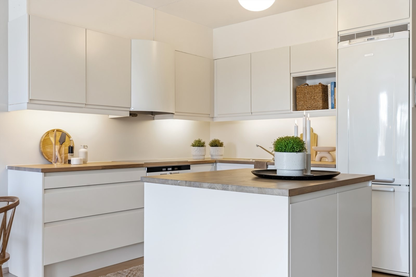 Kjøkkeninnredning med glatte fronter og benkeplate i heltre. Kjøkkenet er utstyrt med kjøl/fryseskap, oppvaskmaskin, platetopp og stekeovn. Galleribilde
