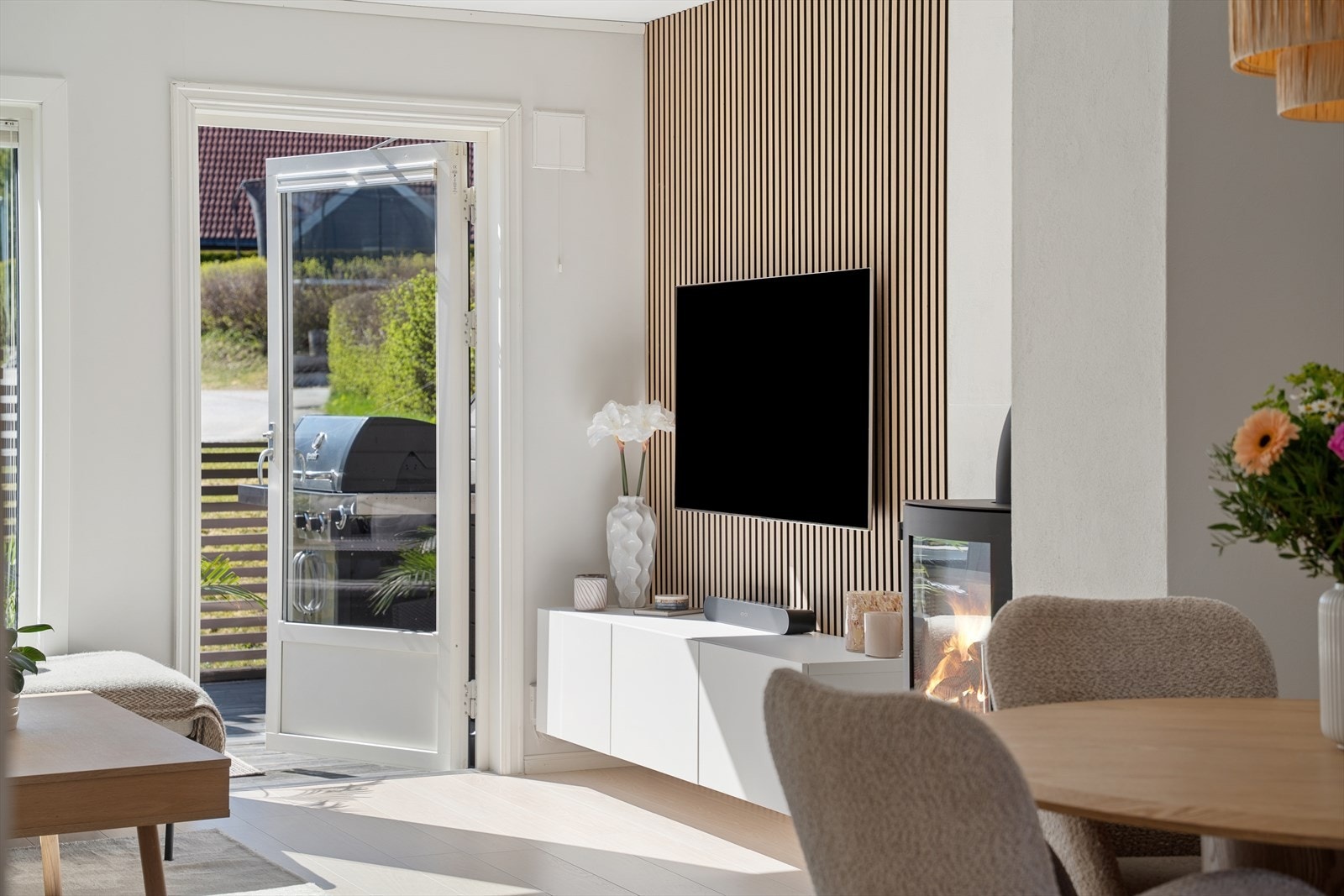 En stilren spilevegg definerer TV-sonen og tilfører rommet en moderne varme. Vedovnen bidrar med ekstra hygge på kalde dager. Galleribilde