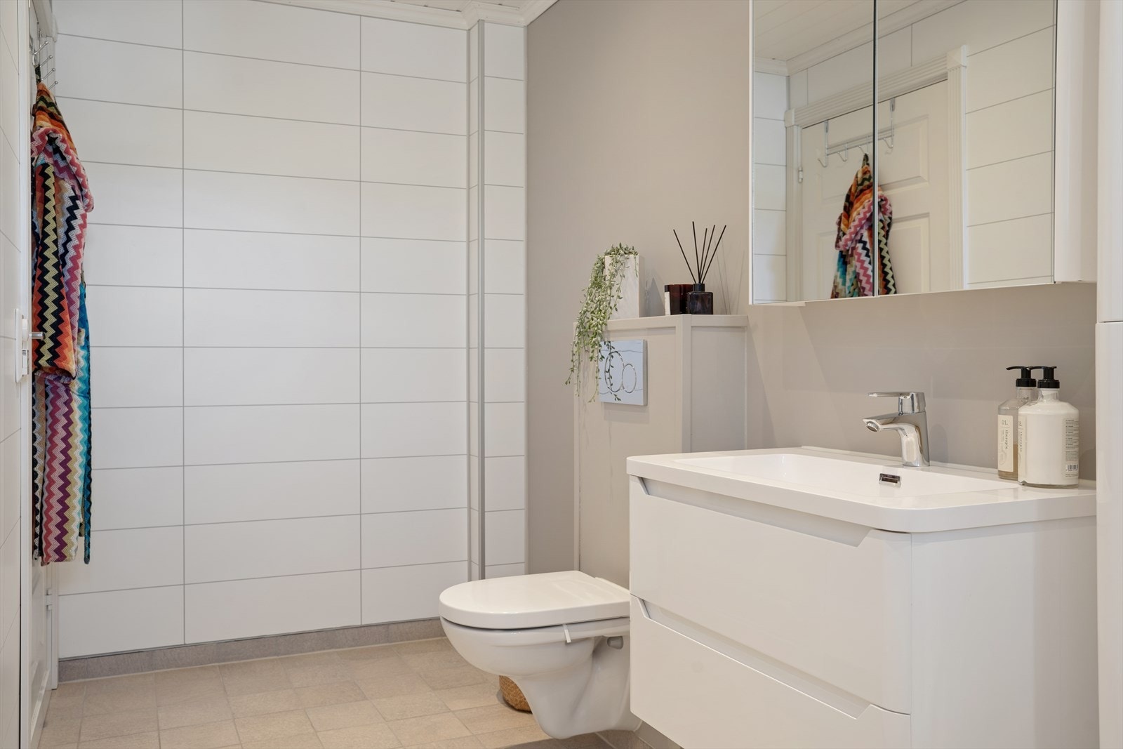 Badet er innredet med veggmontert toalett, servant med underskap og overskap med speil. Veggene har baderomsplater. Galleribilde