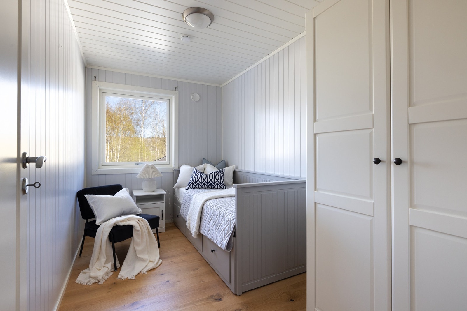 Lyst soverom med panelvegger, vindu som slipper inn naturlig lys og garderobeskap. Galleribilde