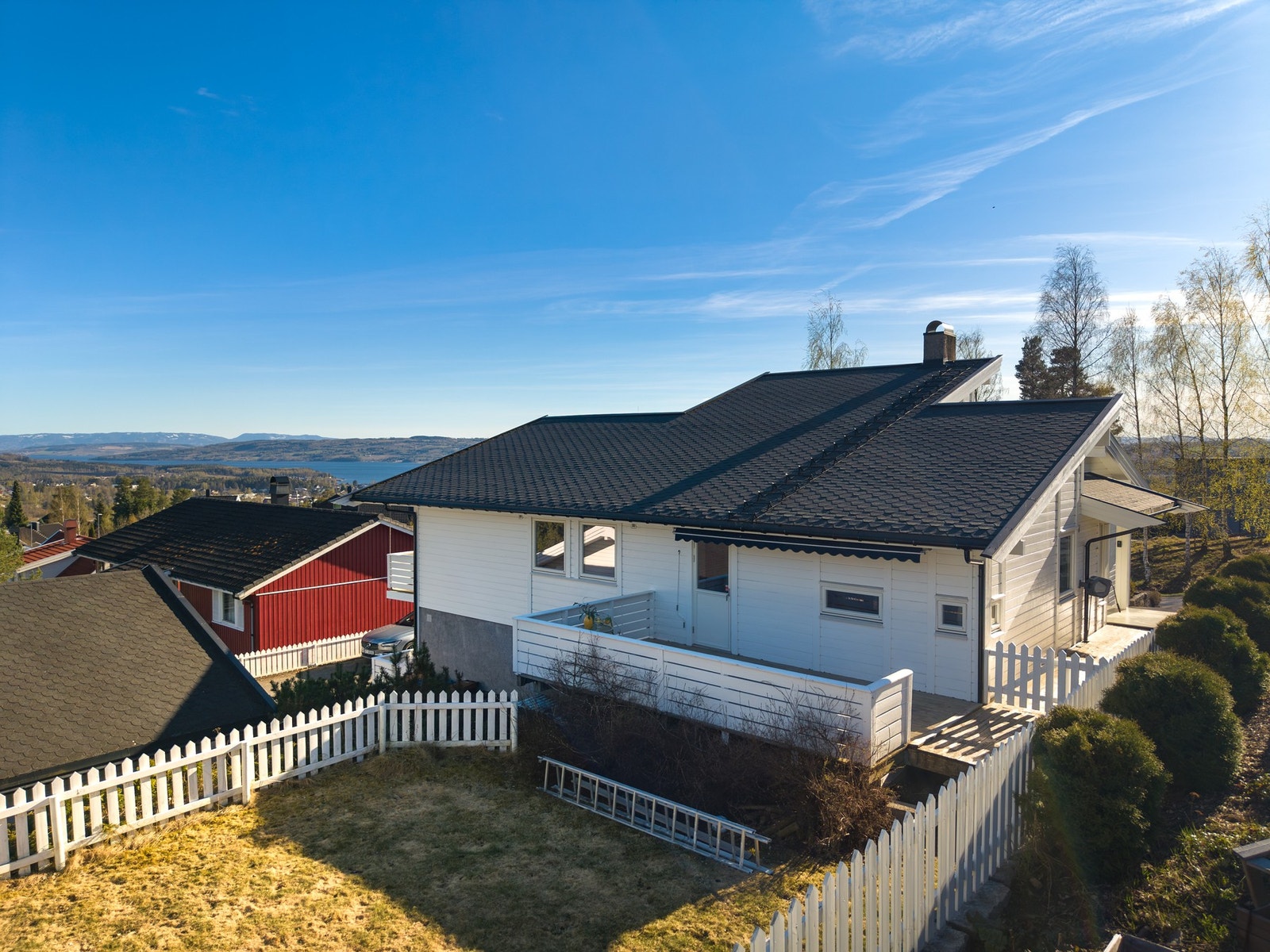 Hvit enebolig med svart tak, inngjerdet hage og utsikt over landskapet. Galleribilde