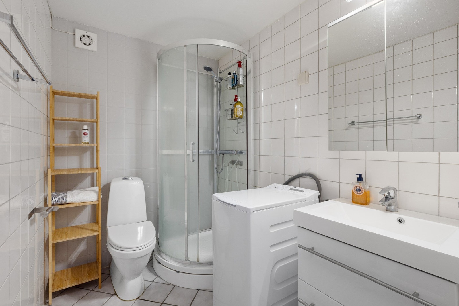 Badet har dusjkabinett, toalett, servant med underskap og vaskemaskin. Flislagte vegger og gulv. (hybel) Galleribilde