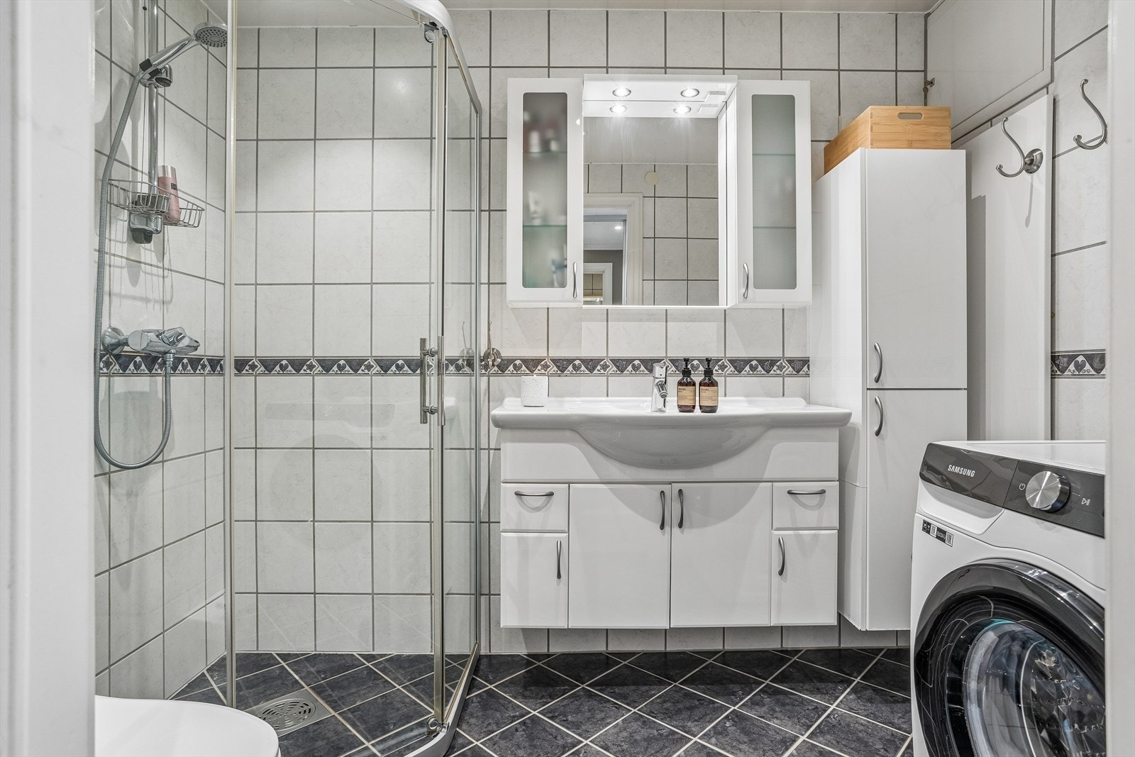 Flislagt bad med varme i gulvet. Rommet er utstyrt med dusjhjørne med glassvegger, vegghengt toalett og opplegg for vaskemaskin. Galleribilde