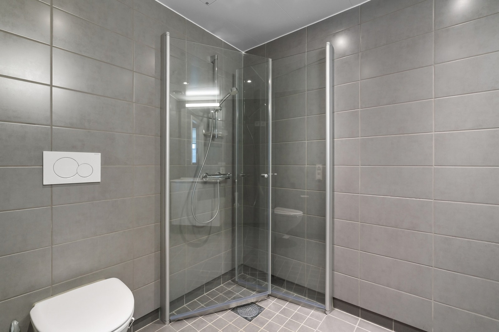 Badet er innredet med vegghengt toalett, dusjhjørne, servantseksjon med skap og speil. Galleribilde