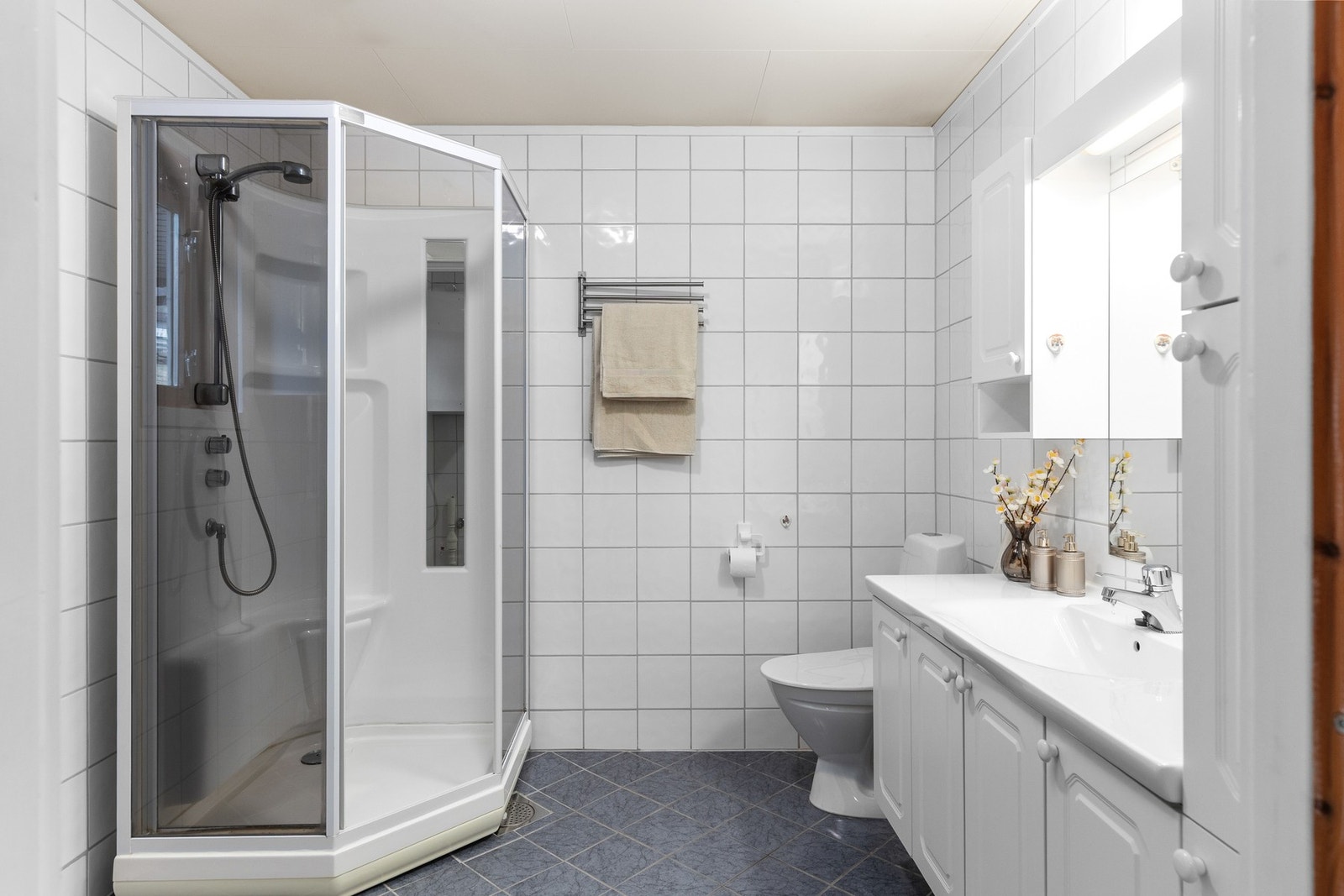 Flislagt baderom med varme i gulv- utstyrt med servant, servantskap, mekanisk avtrekk, wc, opplegg for vaskemaskin og dusjkabinett. Galleribilde