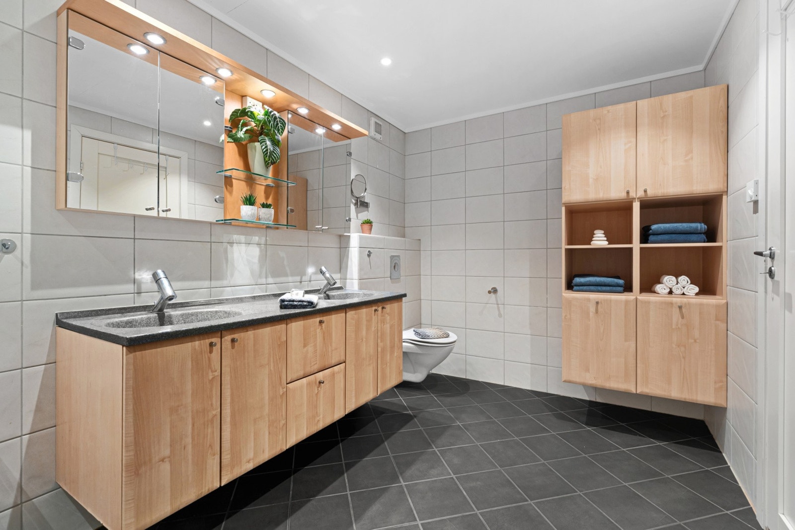 Badet fremstår som romslig og funksjonelt, med flislagte overflater og en stilren innredning. Den brede baderomsinnredningen gir god skap- og benkeplass, og sørger for praktisk oppbevaring i hverdagen. Galleribilde