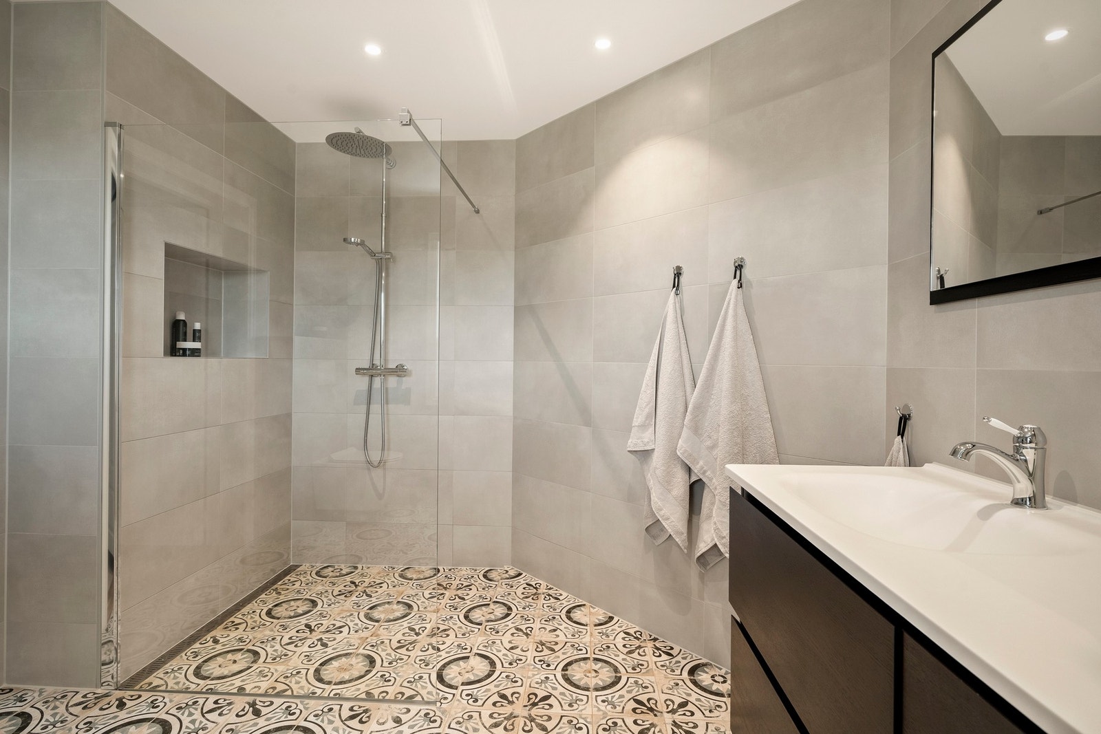Badet er utstyrt med dusj med glassvegg, servantseksjon med skuffer og vask, speil med lys og vegghengt wc. Galleribilde