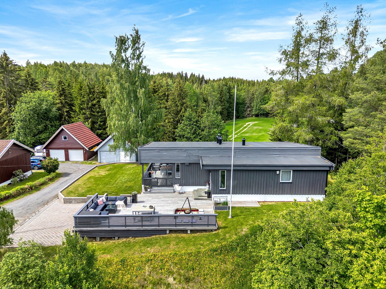 Gruset innkjøring inn til garasjen og belegningsstein på gårdsplass, som leder videre til boligens terrasse og inngangsparti. Galleribilde