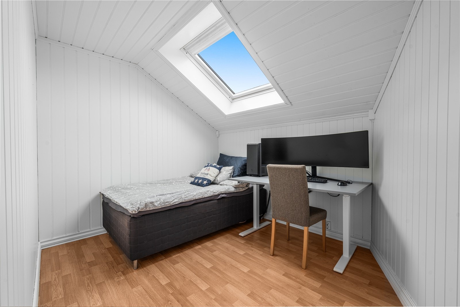 Rom benyttet som soverom på loftet er lyst og trivelig med smart panel på veggene og et stort takvindu. Galleribilde