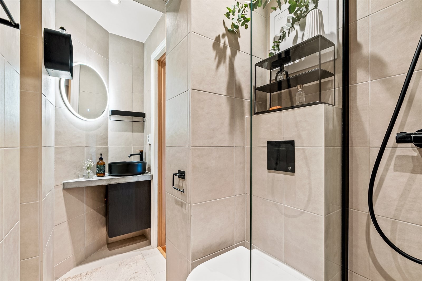 Badet er utstyrt med fliser, har downlights i himlingen og elektrisk gulvvarme. Videre er badet innredet med vegghengt klosett, servant på innredning og speil med lys. Galleribilde