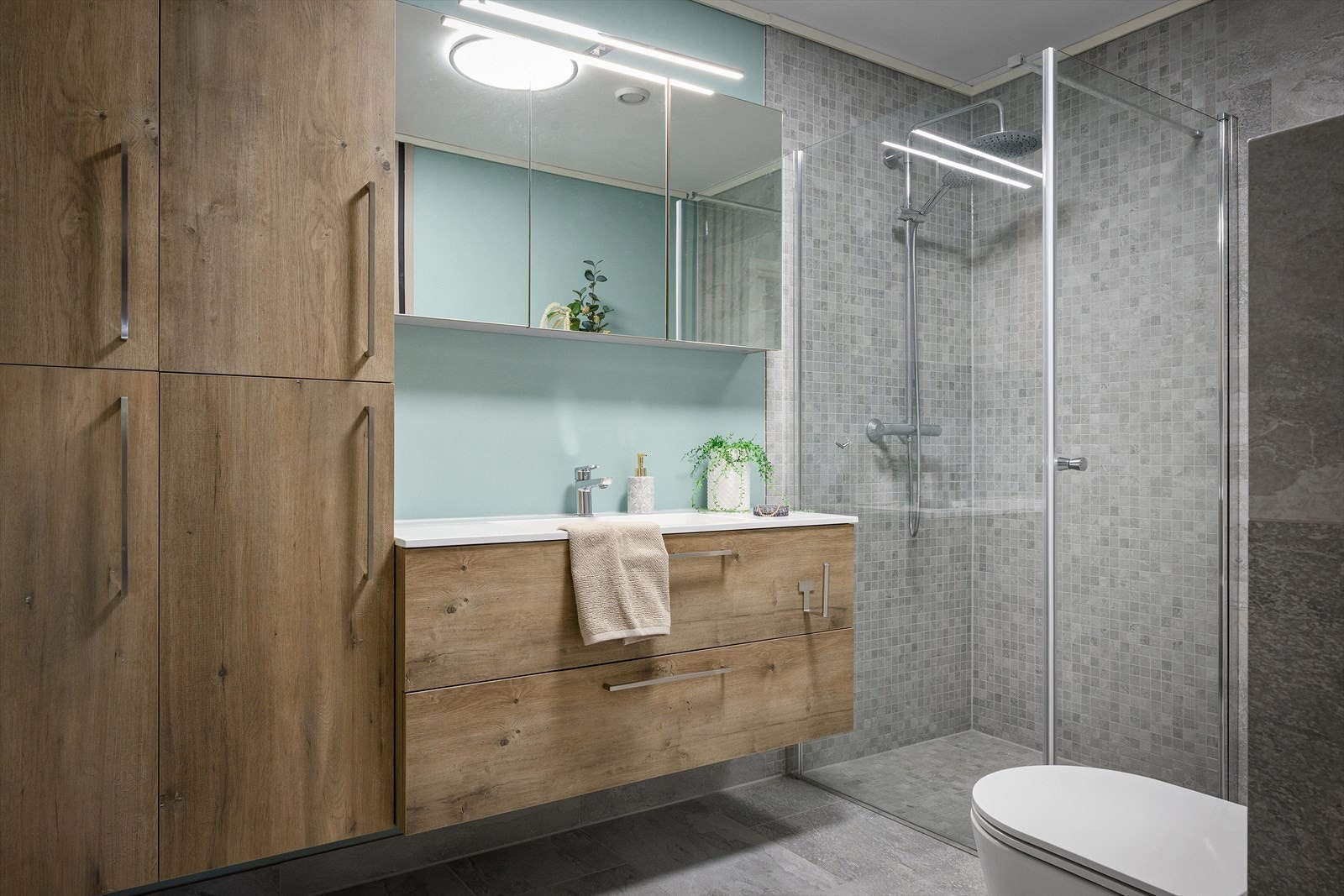 Badet er lekkert med grå fliser, vegghengt toalett, regndusj og dusjvegg i klart glass. Nytt i 2025. Pen innredning med speilskap. Galleribilde