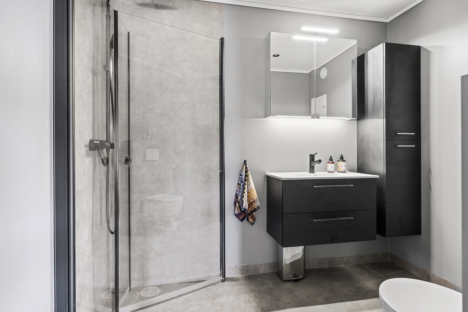 Badet er innredet med vegghengt toalett, dusjhjørne med glassdører og har opplegg for vaskemaskin. Galleribilde