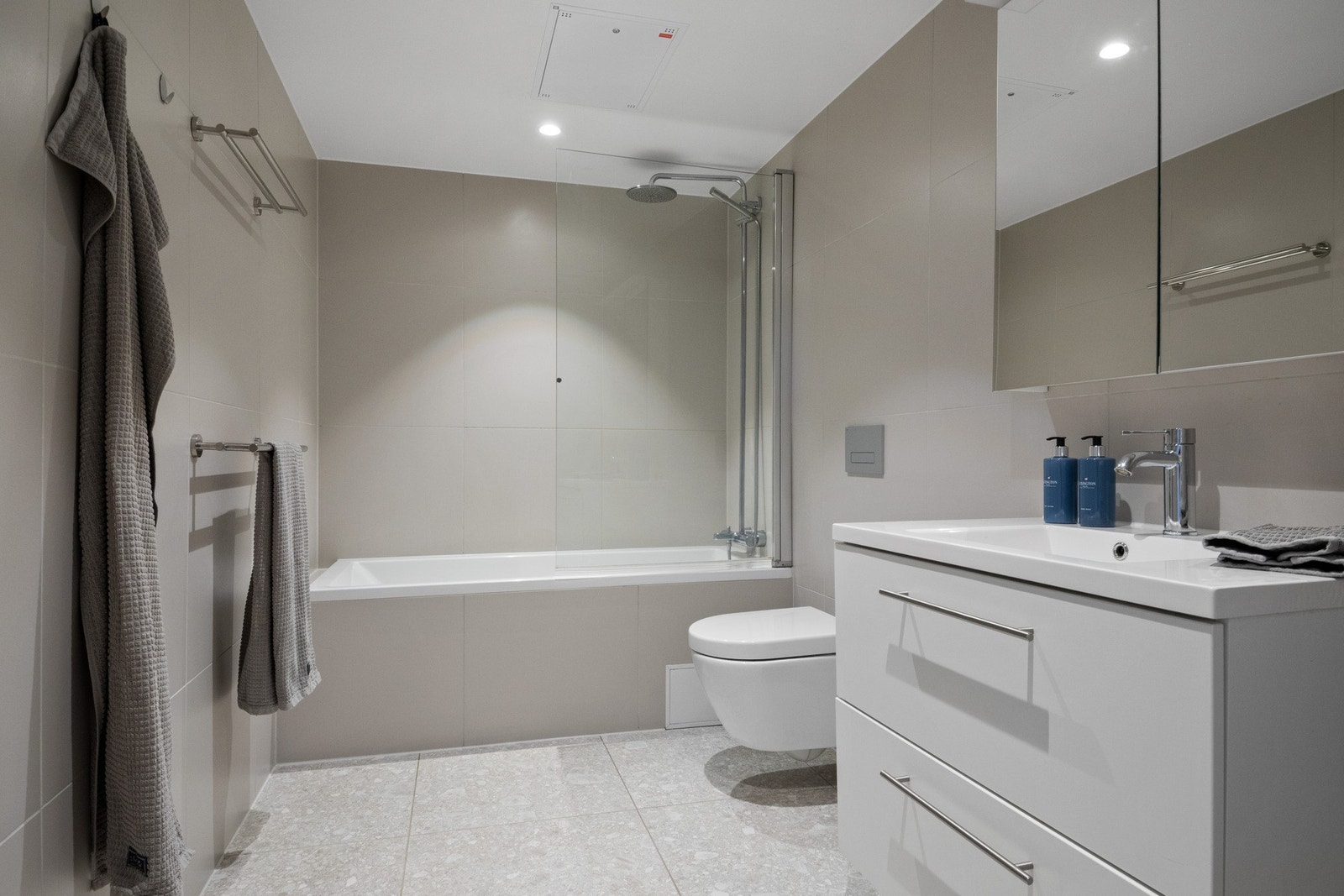 Badet er innredet i en lys og tidløs stil, med store veggfliser i lyse, nøytrale toner og gulvfliser i lys gråbeige utførelse. Galleribilde