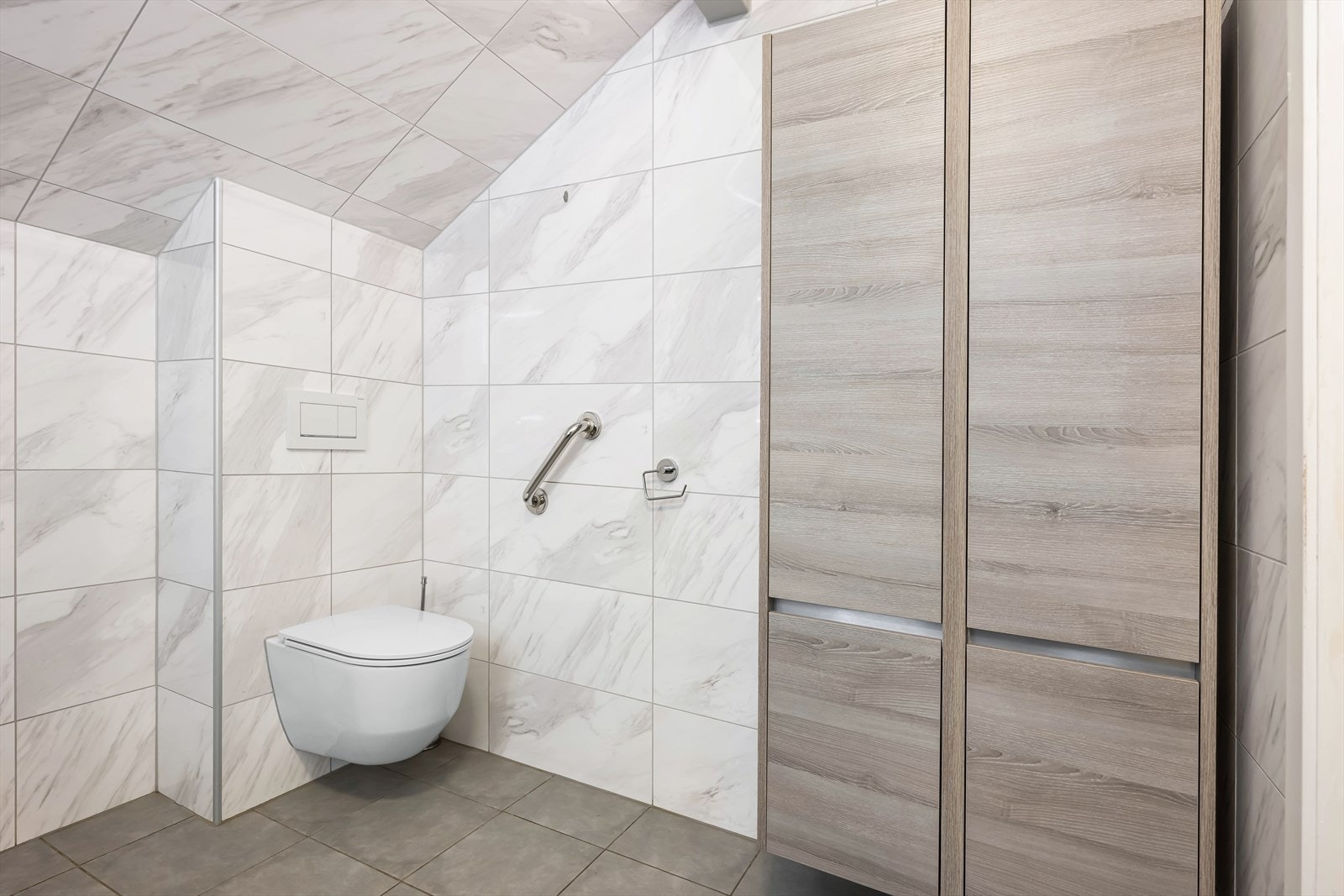 Badet er utstyrt med vegghengt toalett for enklere renhold, samt praktiske høyskap for ekstra oppbevaring. Galleribilde