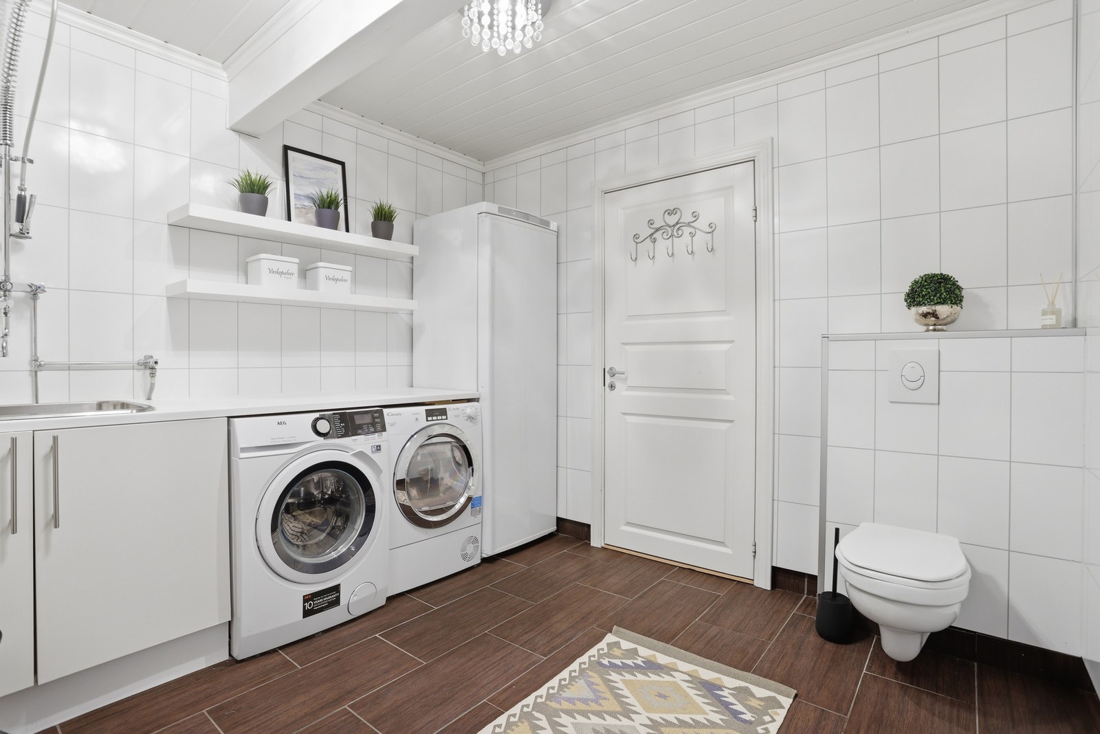 Lyst og moderne vaskerom med flislagte vegger, vaskemaskin, tørketrommel og toalett. Galleribilde
