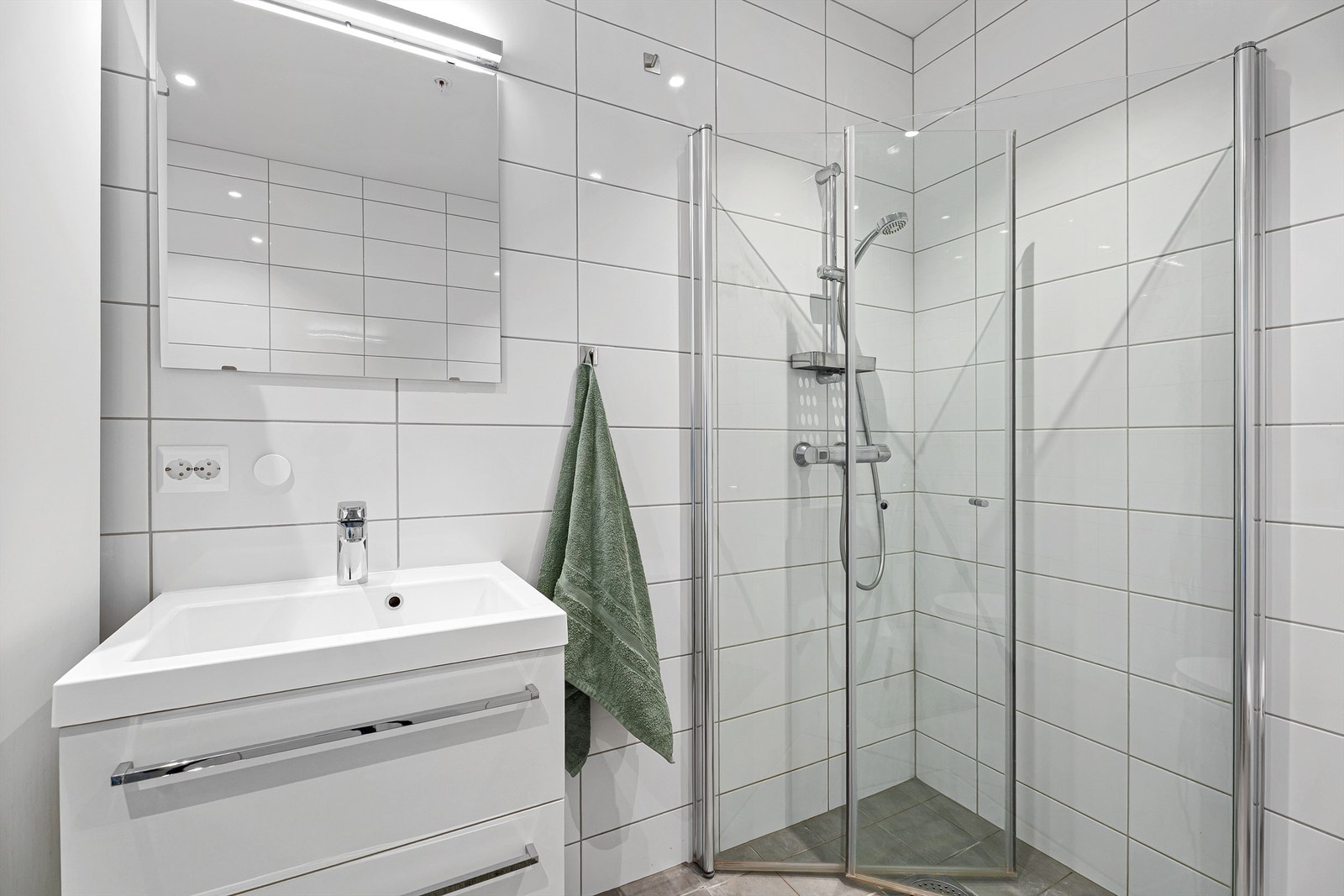 Badet har dusjnisje med innfellbare dører, vegghengt servant med skuffer samt speil med belysning. Galleribilde
