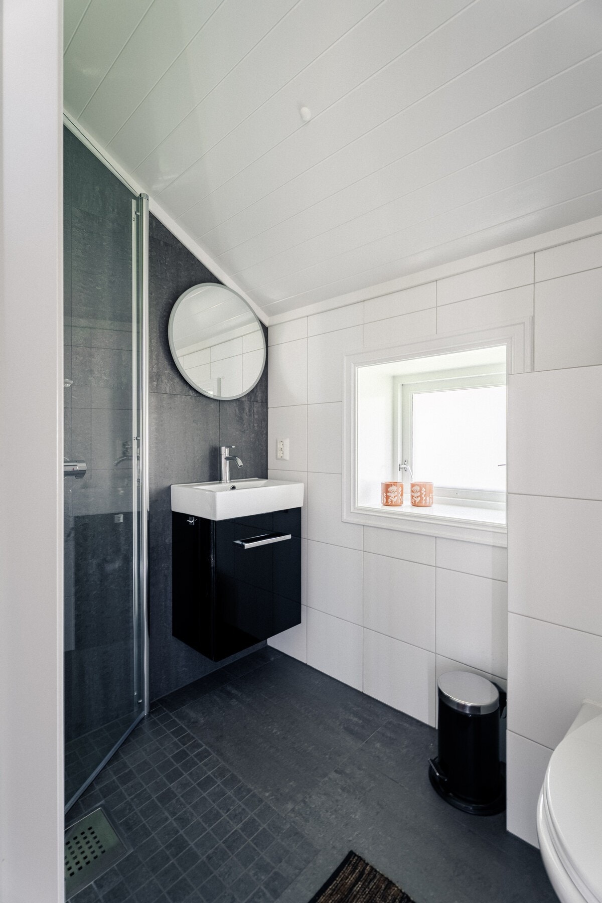 Badet i 1. etasje er fra 2020 og har mørke fliser, dusjhjørne med glassdør, veggmontert servant med servantmøbel og toalett. Galleribilde