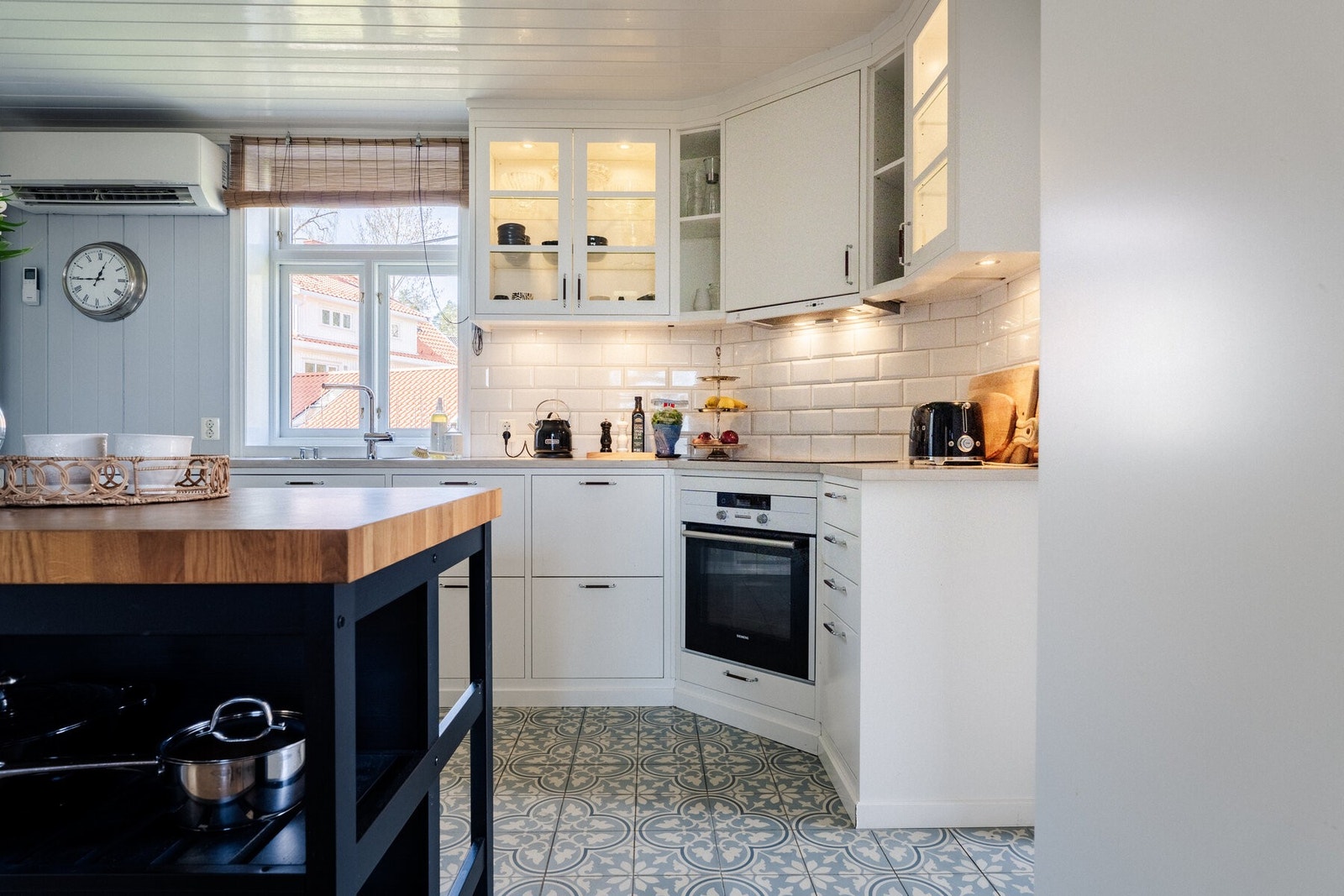 Hvite fronter med glassskap, mønsterfliser i blå-grått på gulvet, hvite ubåtsfliser på veggen. Galleribilde