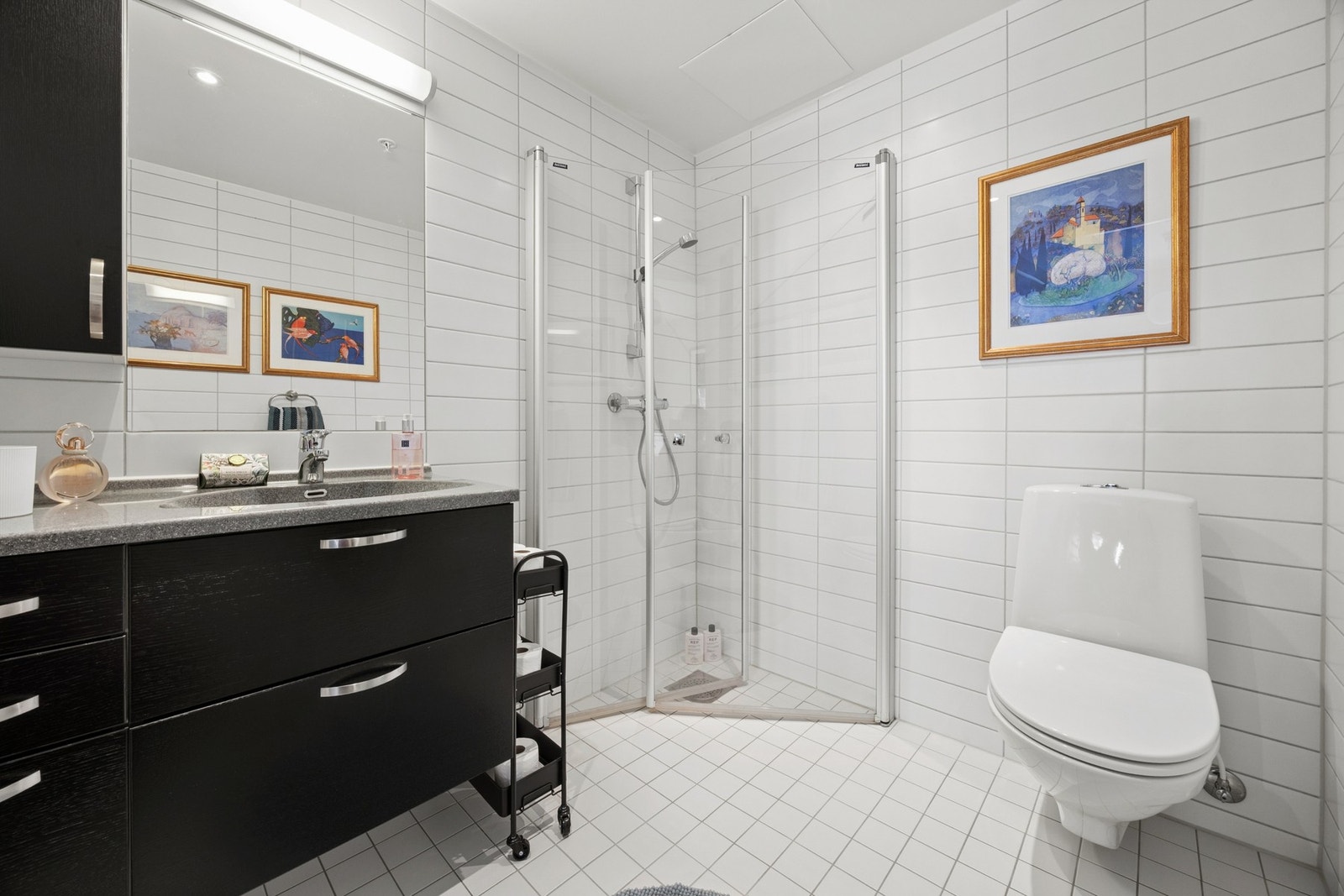 Badet er innredet med servantskap med oppbevaringsplass, vegghengt toalett og dusjhjørne med glassdører. Galleribilde