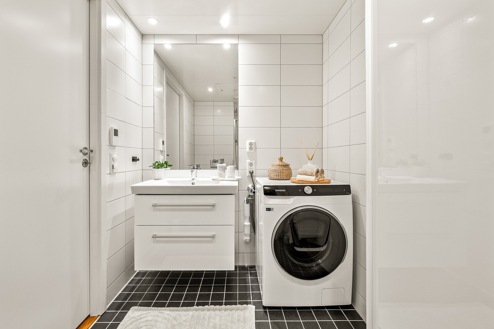 Baderomsinnredningen har hvite, glatte fronter og består av en toppmontert servant på benkeseksjon, høyskap og et speil. Videre har badet et vegghengt toalett og et dusjhjørne. Galleribilde