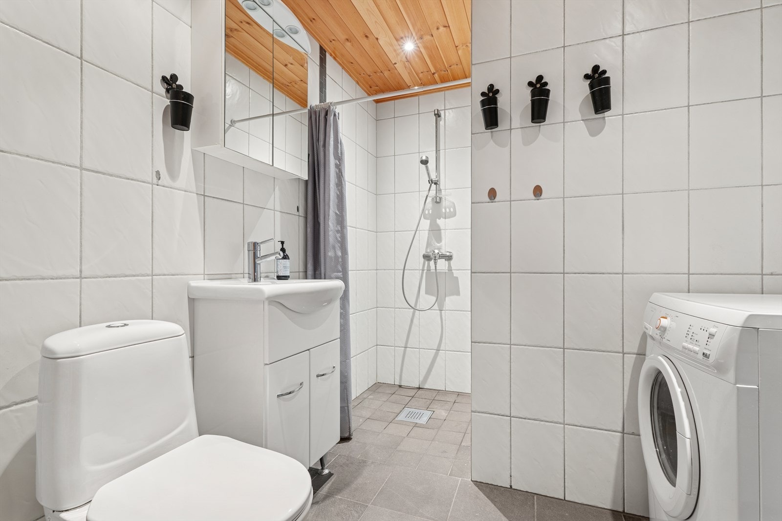 Badet er videre innredet med baderomsinnredningen, gulvmontert toalett, dusj i nisje med forheng og opplegg for vaskemaskin. Galleribilde