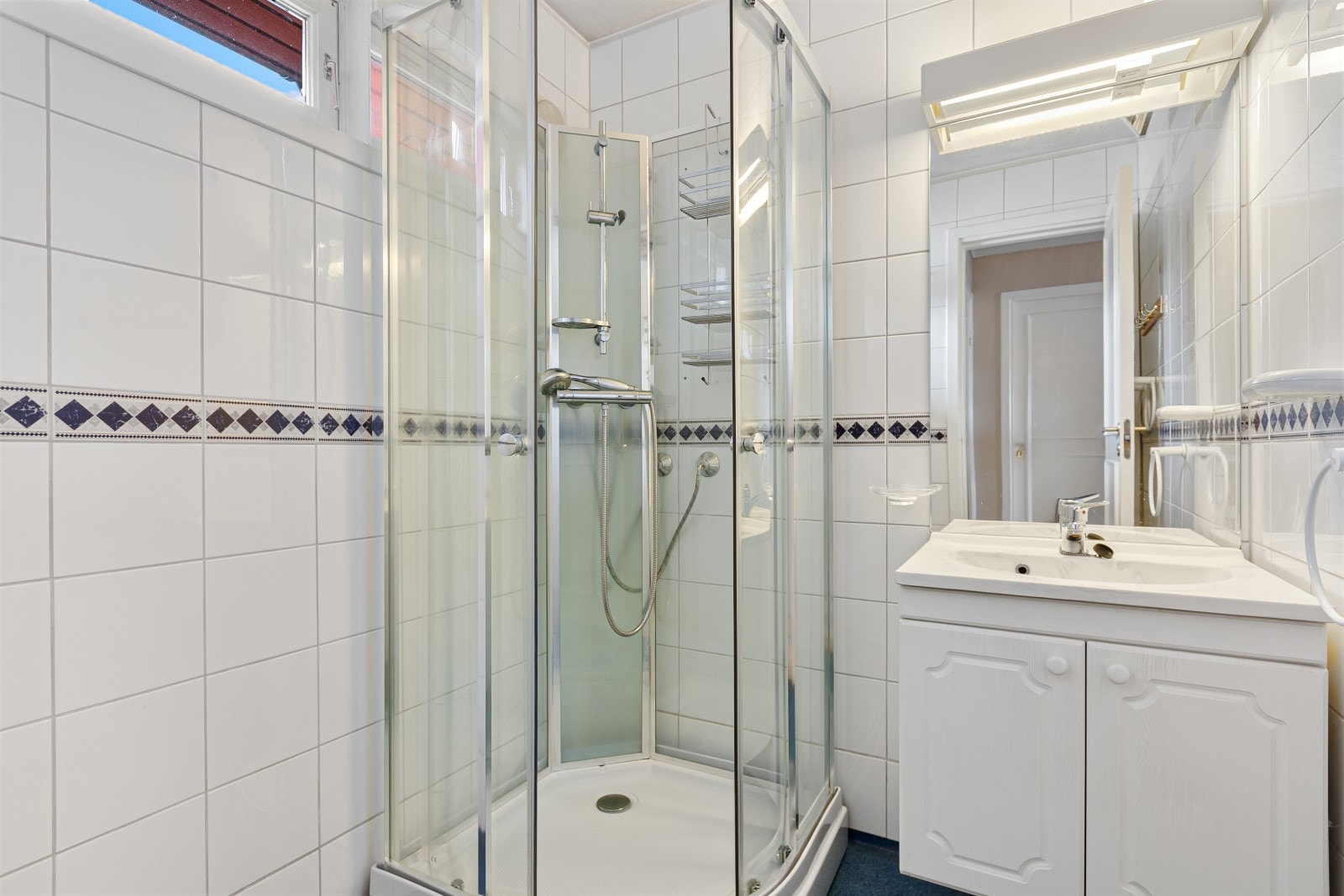 Badet er innredet med servant, dusjkabinett, våtromsbelegg på gulv og keramiske fliser på vegg. Galleribilde