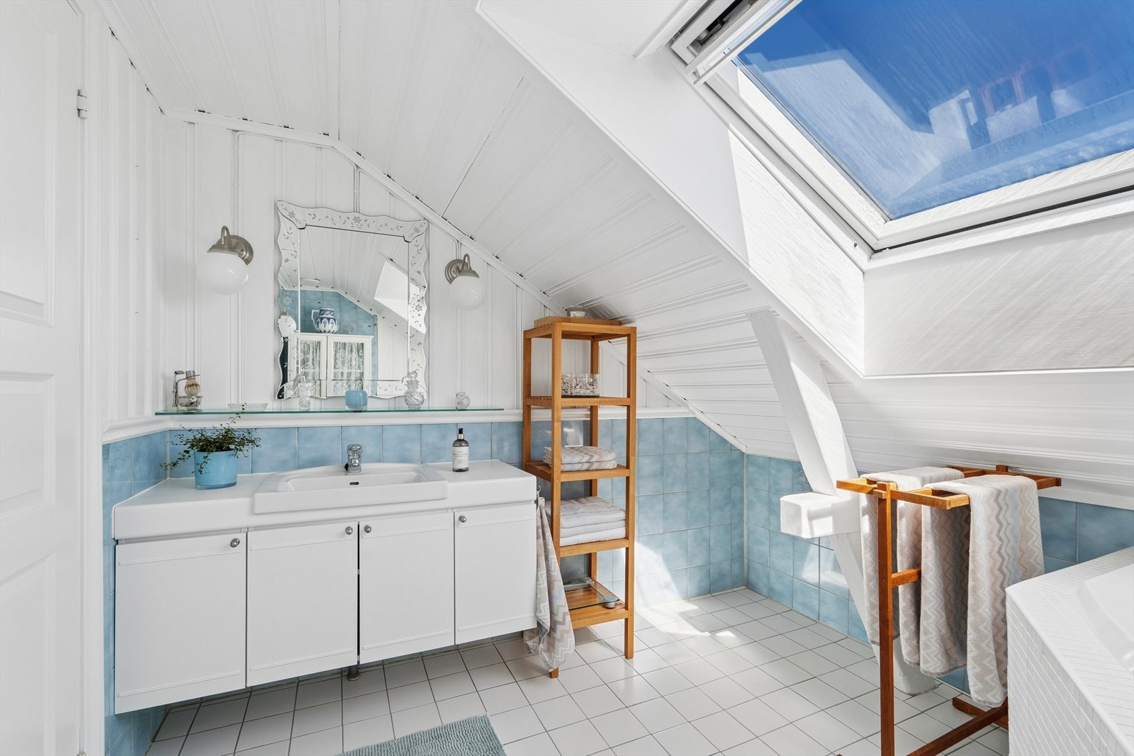 Badet (ukjent alder) har flislagt gulv med varmekabler. Fliser/panel på vegger. Rommet er innredet med et hjørnebadekar, toalett og baderomsinnredning med nedfelt servant. Naturlig ventilasjon. Et takvindu gir rikelig med dagslys. Galleribilde