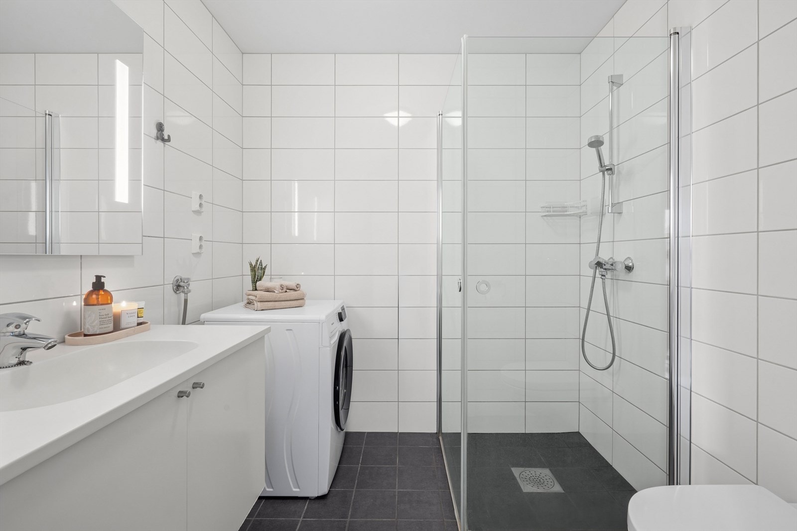 Flislagt baderom på 4,1 m² utstyrt med blant annet innfellbare dusjvegger, opplegg for vaskemaskin/tørketrommel og vegghengt klosett. Galleribilde