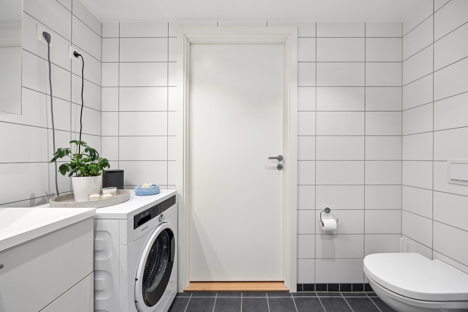 Baderomsinnredning består av dusjhjørne med innfellbare glassdører, servant med underskap med slette fronter, og overskap med speildel og lys. Det er opplegg og plass for vaskemaskin. Galleribilde