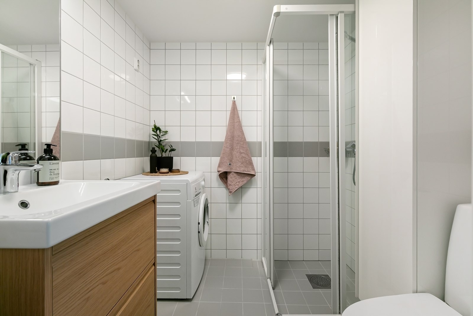 Delikat bad med dusjhjørne, servant med skuffer, wc, speil og opplegg for vaskemaskin og tørketrommel. Galleribilde
