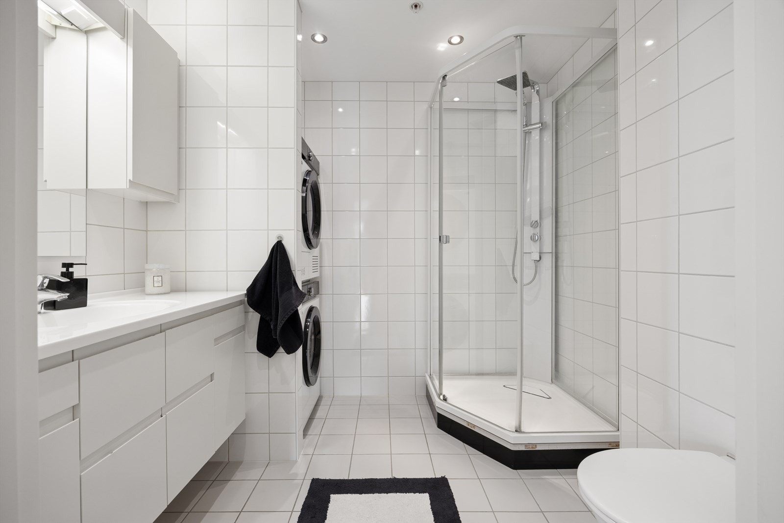 Badet har flislagt gulv, lys baderomsinnredning med skuffer, spotter i tak samt opplegg for vaskemaskin og tørketrommel. Galleribilde