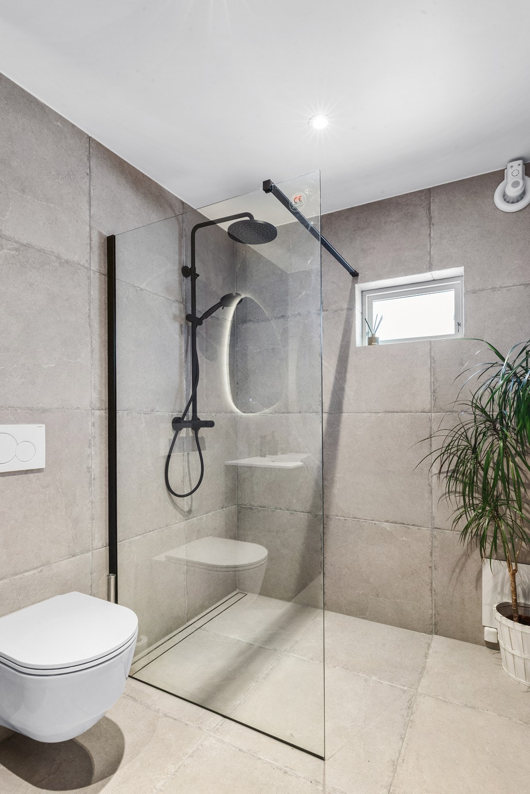 Badet har fliser på gulv og vegger, vegghengt toalett og et moderne dusjhjørne. Galleribilde