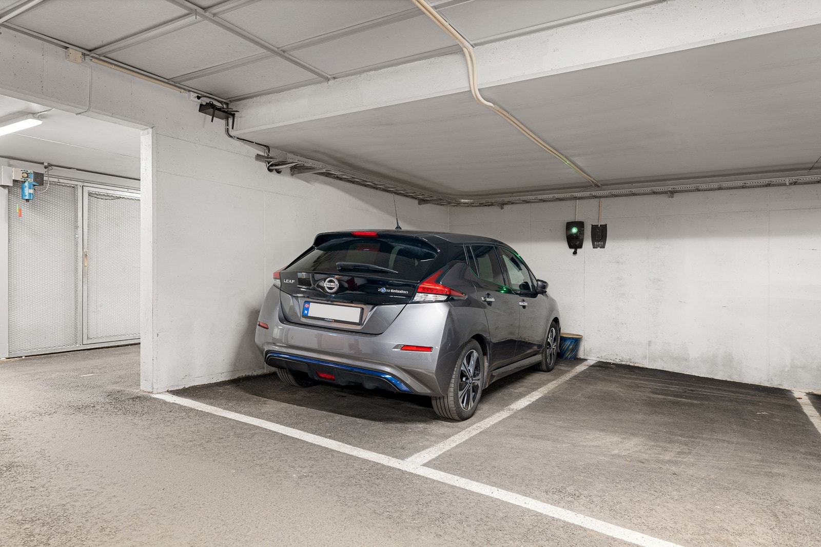 Det medfølger to parkeringsplasser ved siden av hverandre. Den ene plassen er utstyrt med elbillader, plassert slik at den kan benyttes fra begge plassene. Galleribilde