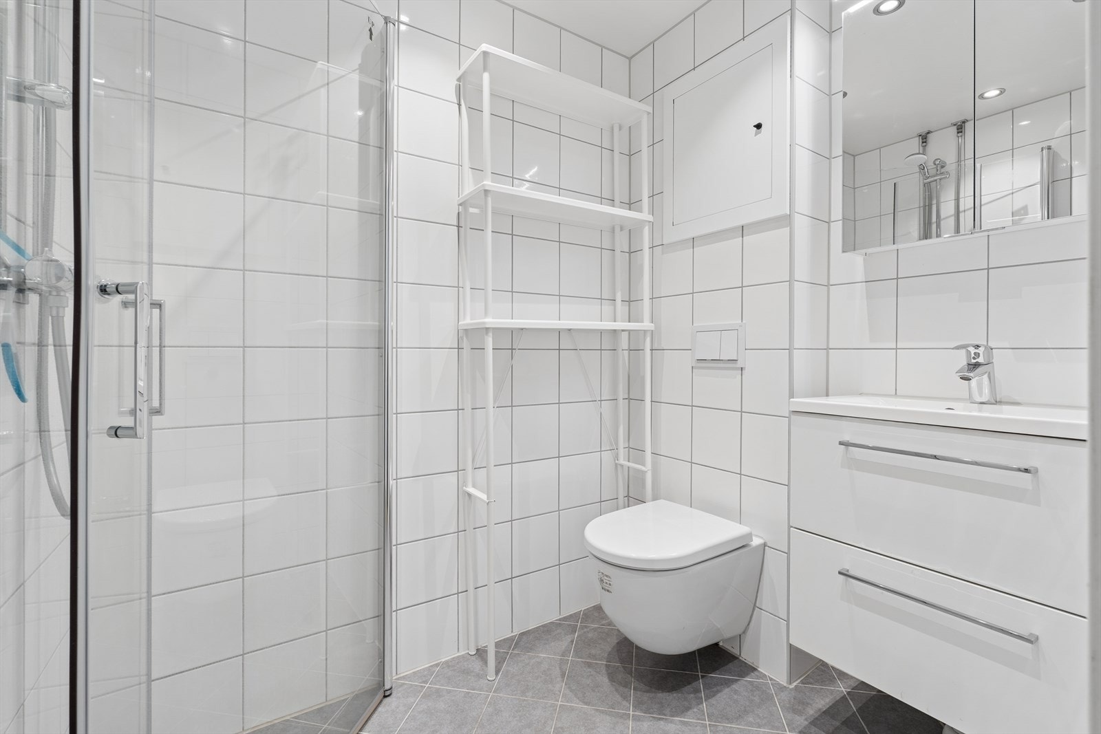 Badet er utstyrt med dusjhjørne, vegghengt toalett og en moderne baderomsinnredning. Galleribilde