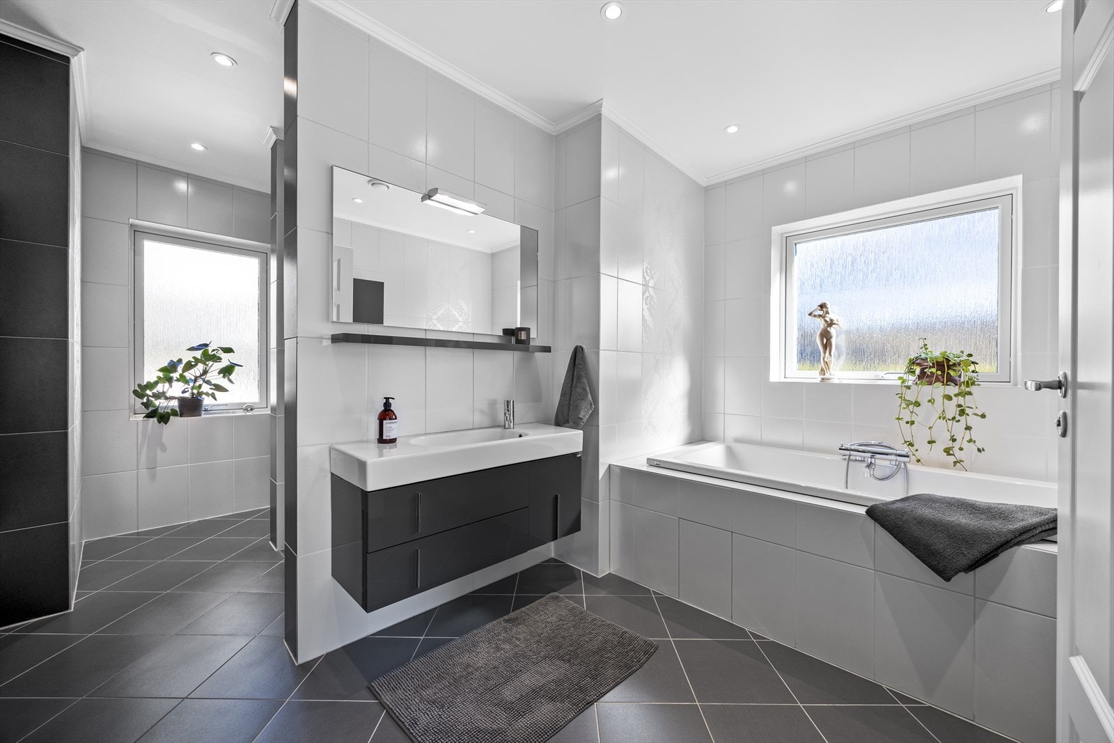 Hovedbadet har fliser til tak, downlights i tak, bred baderomsinnredning med overspeil, wc, stor skjermet dusjnisje og innebygget badekar. Galleribilde
