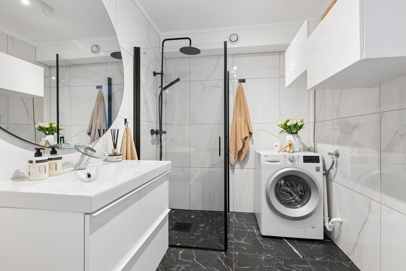 Delikat og praktisk bad utstyrt med moderne servantskap, dusjhjørne i glass og oppstillingsmuligheter for vaskemaskin. Galleribilde