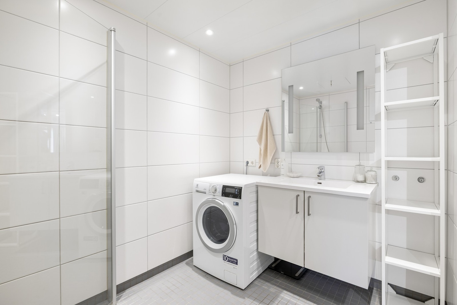 Badet er utstyrt med elektriske varmekabler i gulv, innfellbare dusjdører i glass og kran/avløp for vaskemaskin. Galleribilde