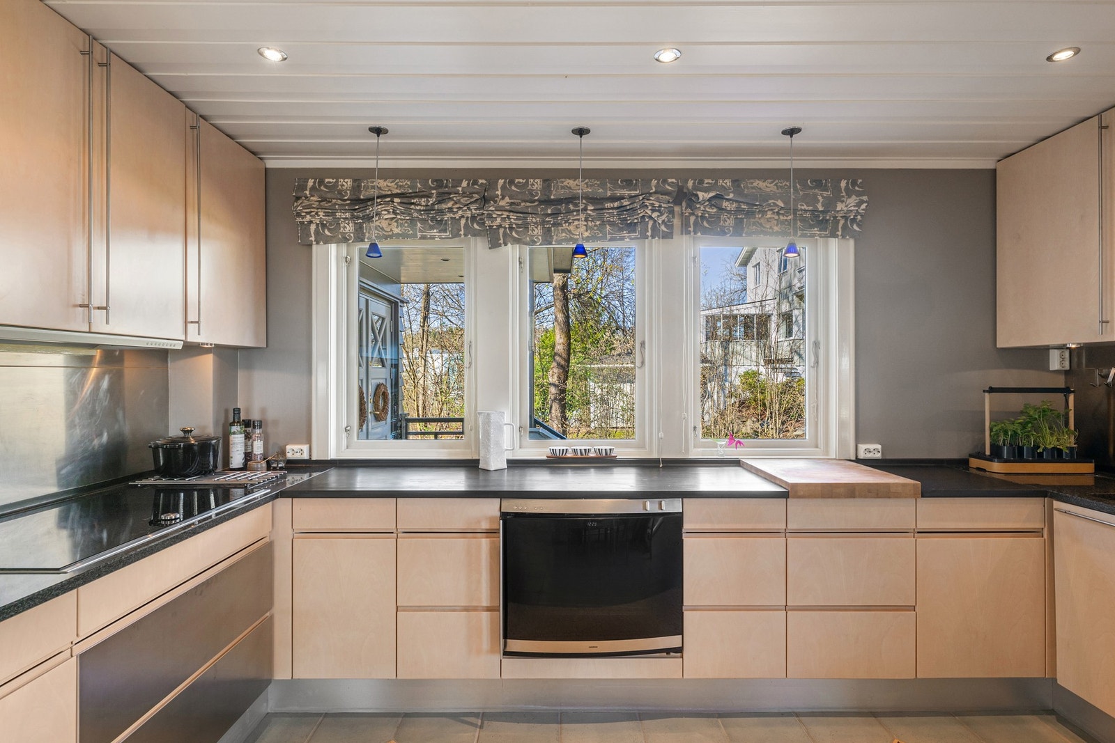 Rustfrie stålplater over benker. Integrerte hvitevarer med Gaggenau stekeovn og NEFF oppvaskmaskin. Gaggenau ventilator i overskap. Galleribilde