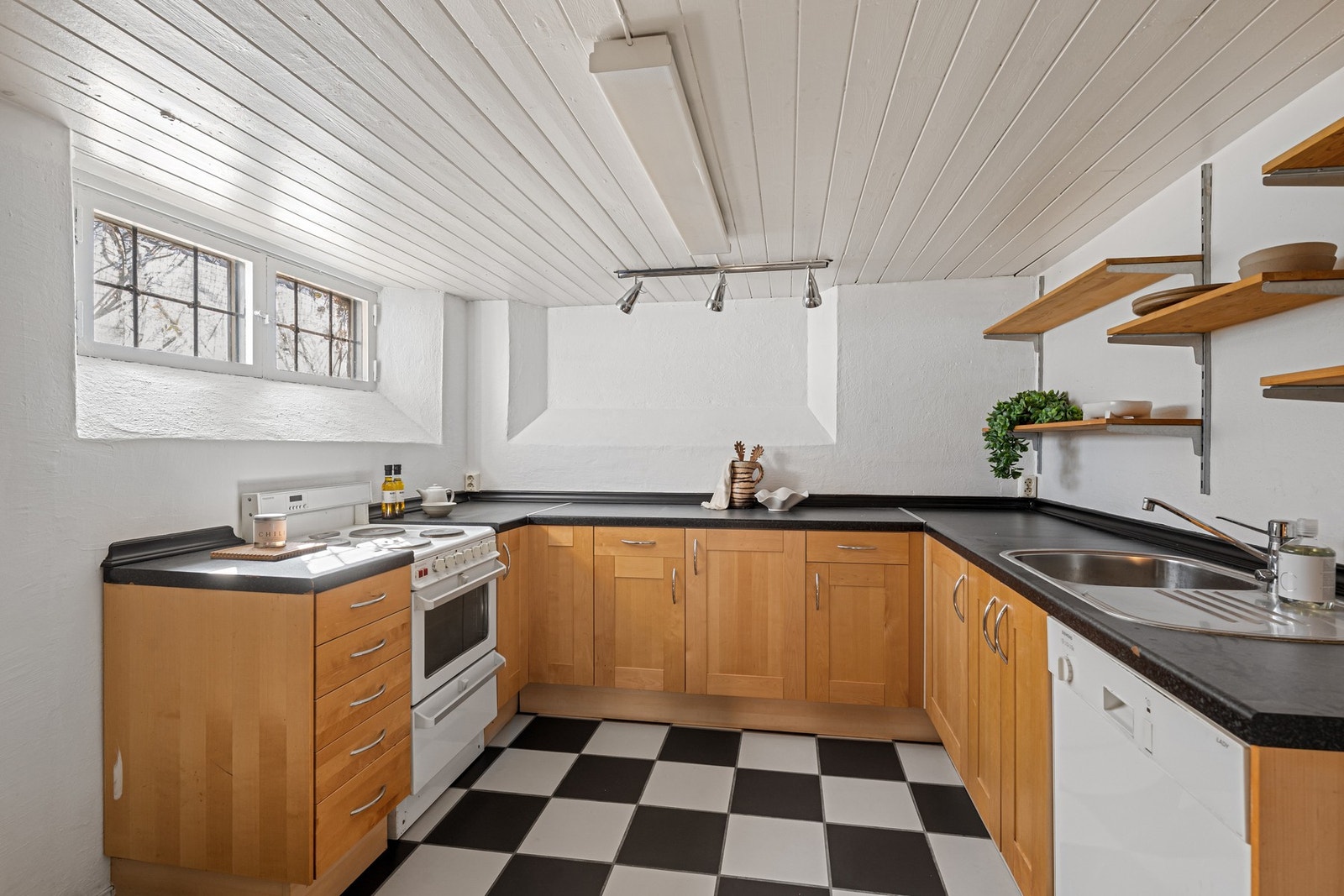 Innredning med finerte fronter, laminat benkeplate med nedfelt vaskekum. Plass for frittstående komfyr, oppvaskmaskin og kjøleskap. Åpne hyller på vegg. Galleribilde