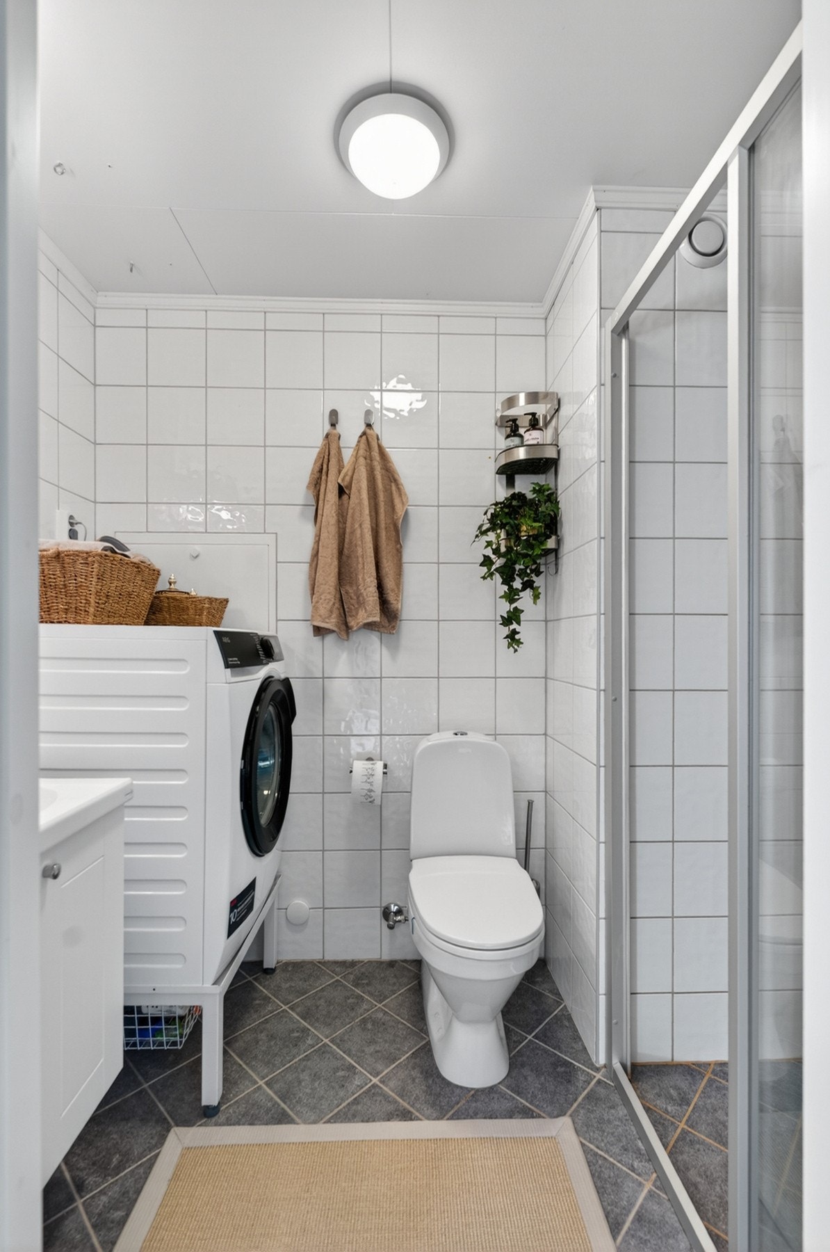 Flislagt bad med gulvvarme, og en baderomsinnredning bestående av benkeskap med profilerte fronter, dusj på gulv, gulvstående klosett, servant og opplegg for vaskemaskin. Galleribilde