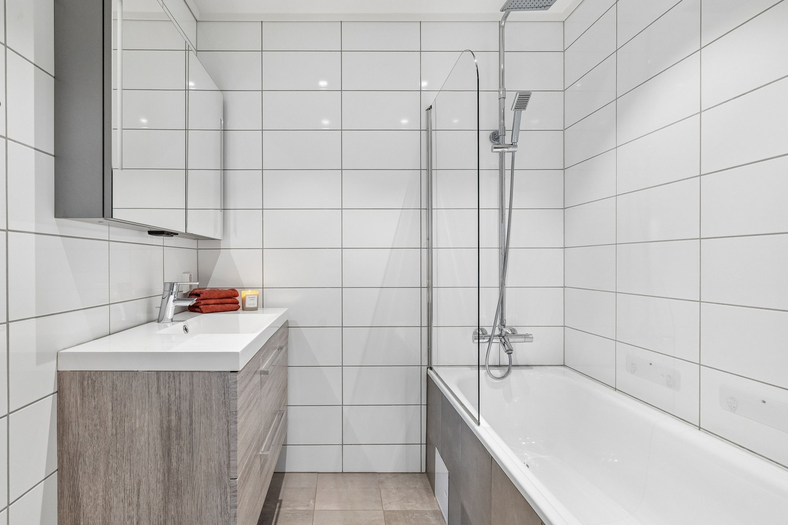 Badet har vegghengt toalett, badekar med dusj, servantinnredning med underskuffer og speilskap med lys Galleribilde
