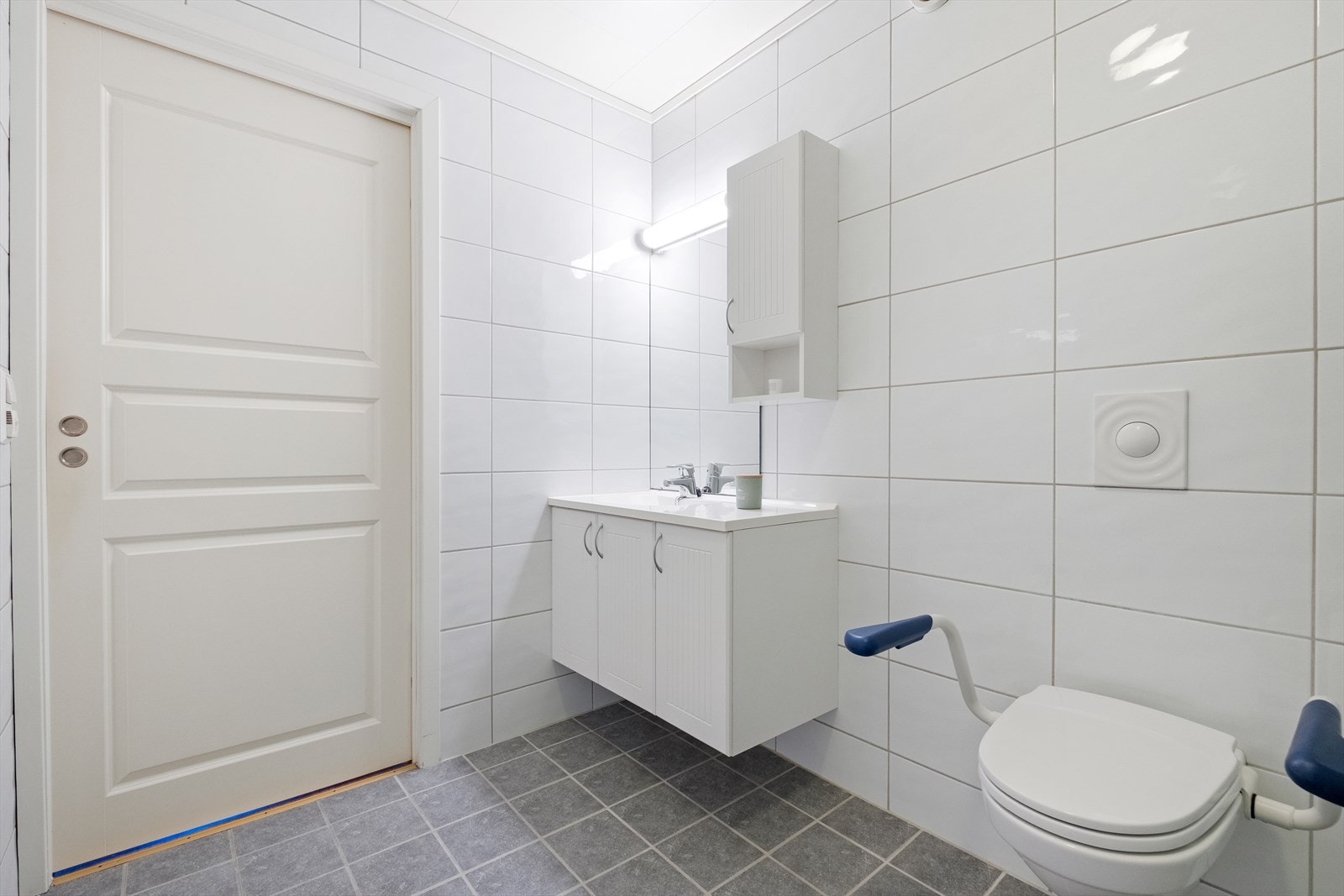 Badet er utstyrt med vegghengt toalett, dusjvegger av glass, servantskap med heldekkende servant, overskap og speil. Galleribilde