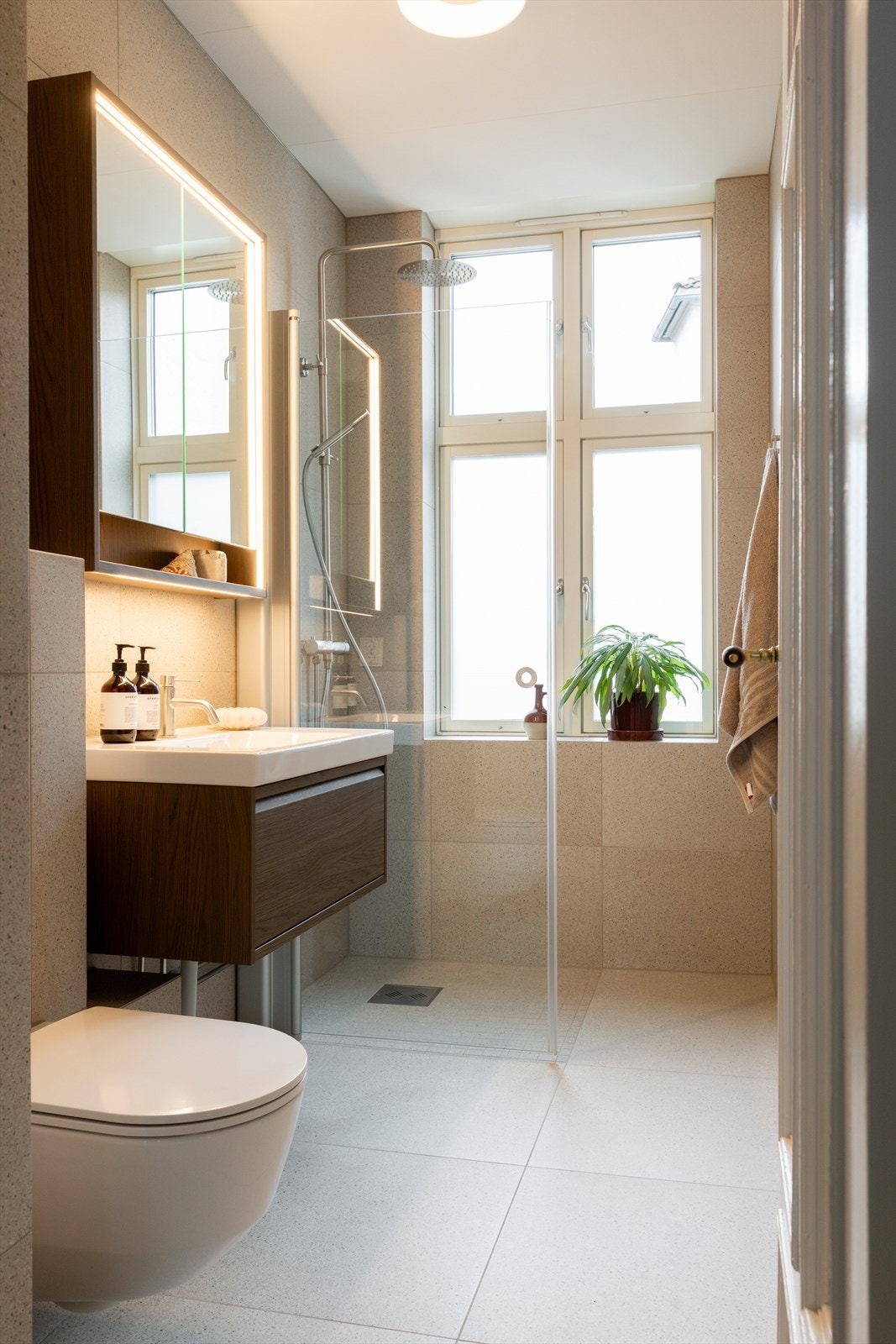 Badet er innredet med servant, speilskap med belysning, vegghengt toalett og innfellbar dusjdør i herdet glass. Galleribilde
