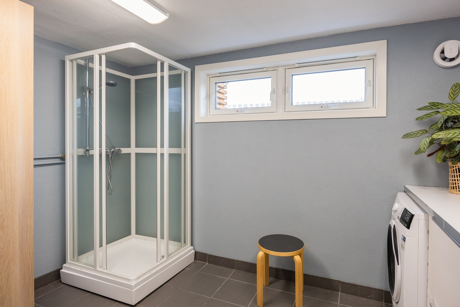 Rommet har fliser på gulv. Her er innredning med utslagsvask og opplegg for vaskemaskin og tørketrommel, toalett og dusjkabinett. Galleribilde