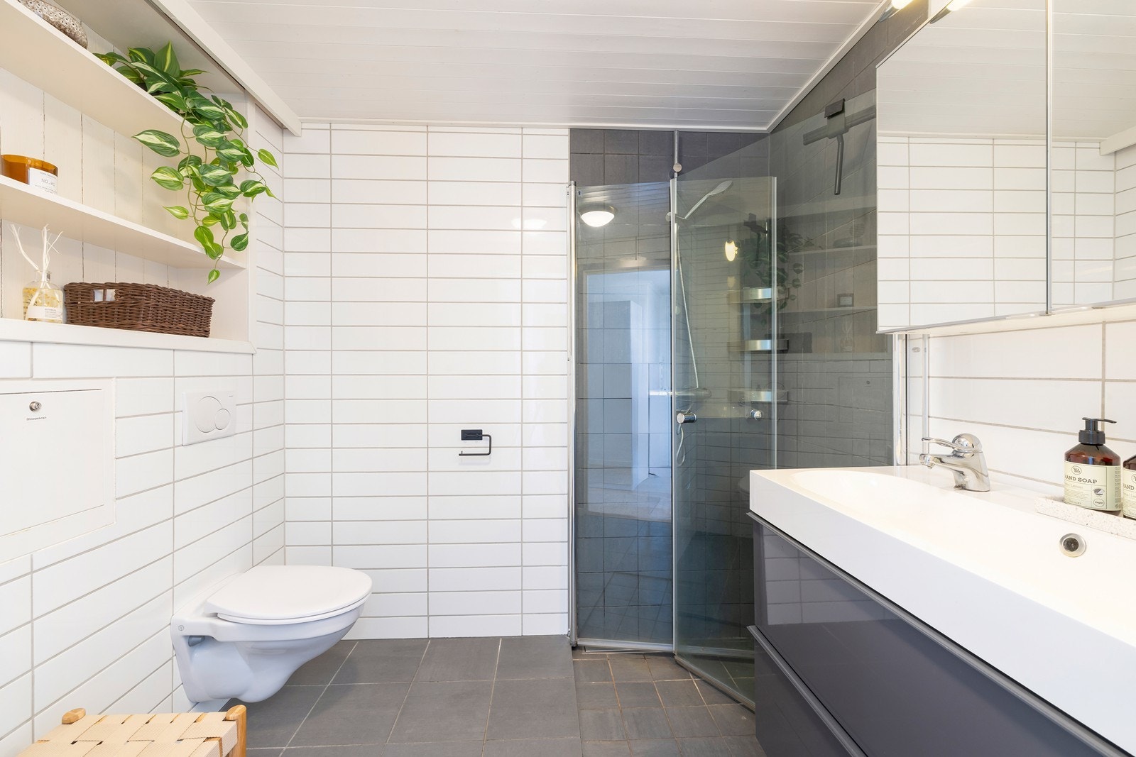 Badet framstår som pent og moderne med vegghengt klosett, innfellbart dusjhjørne i glass og vegghengt dobbelservant med overskap. Galleribilde