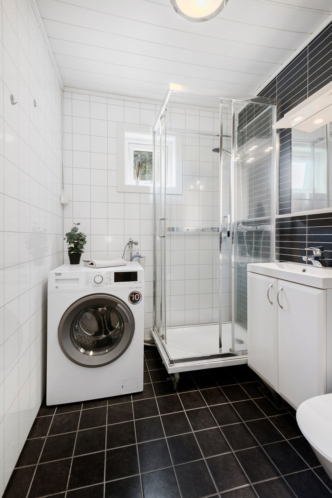 Flislagt bad som er utstyrt med dusjkabinett, servant med underskap og opplegg vaskemaskin. Galleribilde